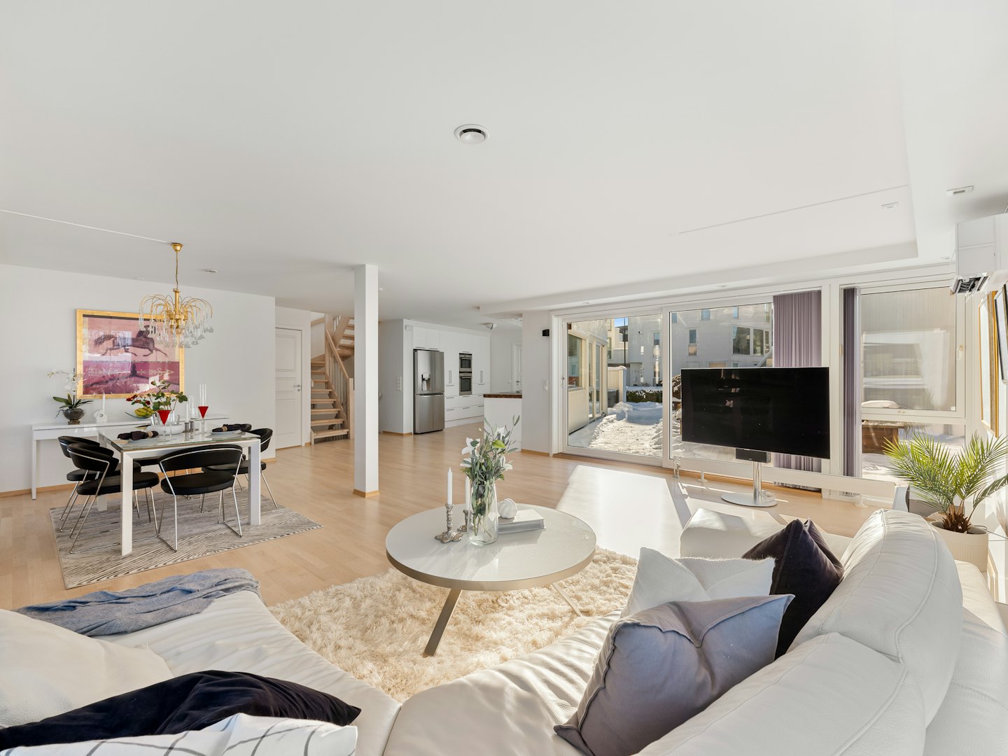 Modern living and dining room with white furniture and wooden floors.