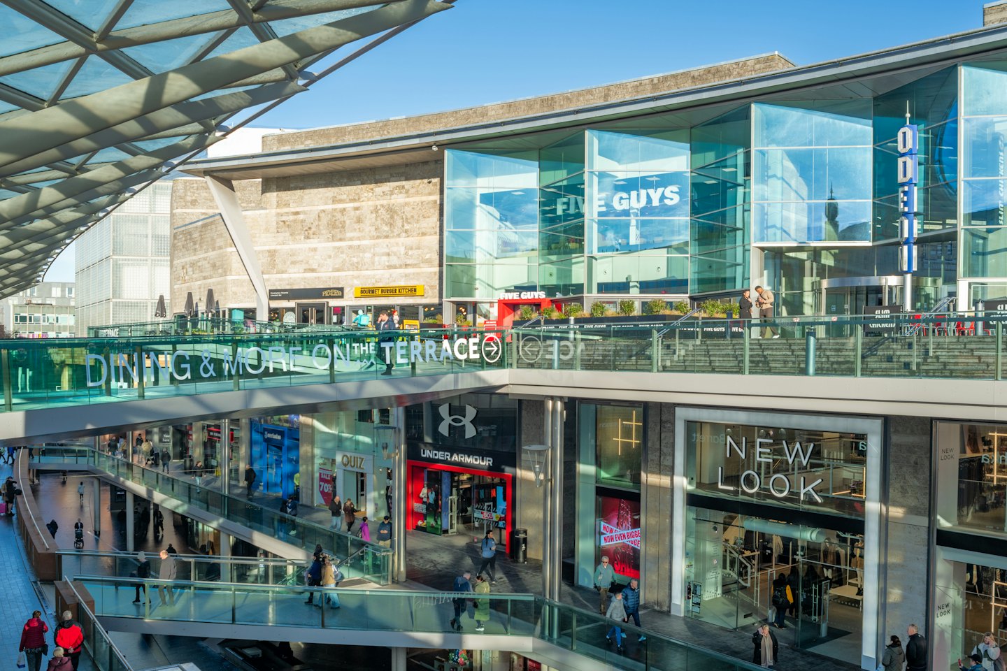 Shoppers and diners at a multi-level outdoor shopping and dining complex.